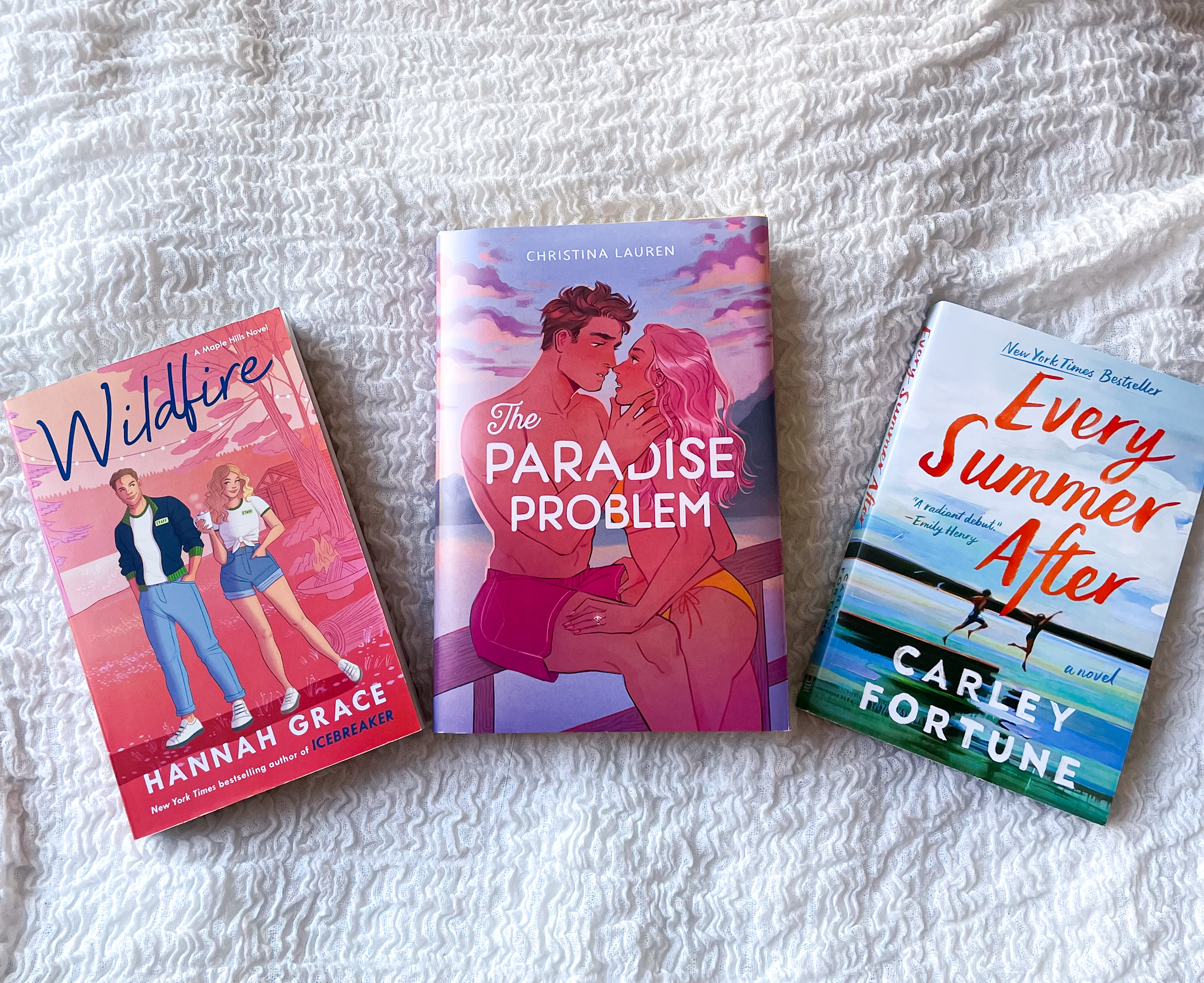 June Book Haul featuring three books on a white textured surface: Wildfire by Hannah Grace, The Paradise Problem by Christina Lauren, and Every Summer After by Carley Fortune, showcasing vibrant covers perfect for summer reads.